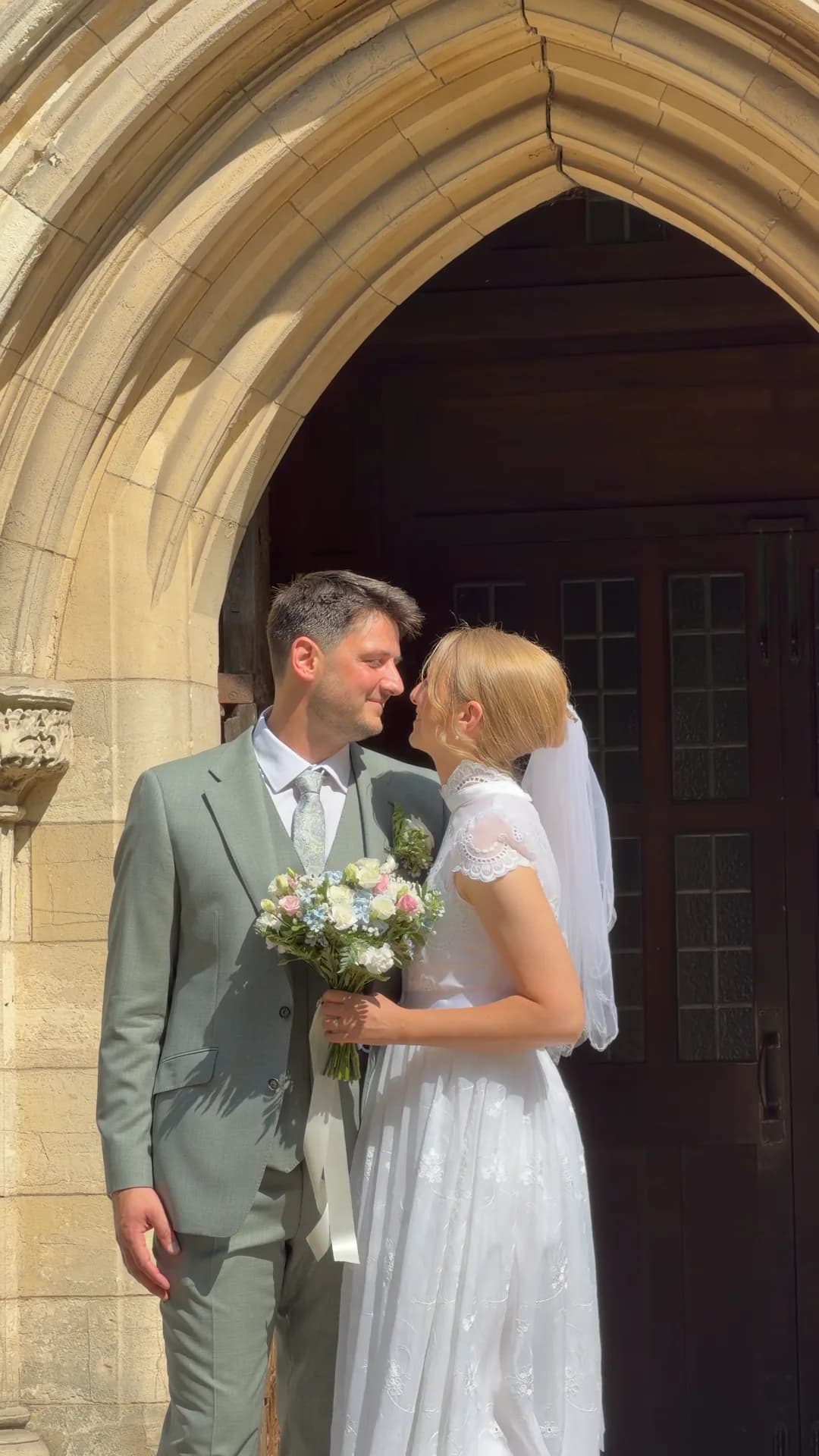 Bride and groom sharing a moment beneath a stone church archway, filmed vertically